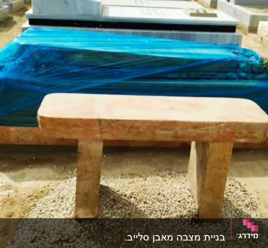 קבר מכוסה בניילון כחול עם ספסל אבן מלפנים
